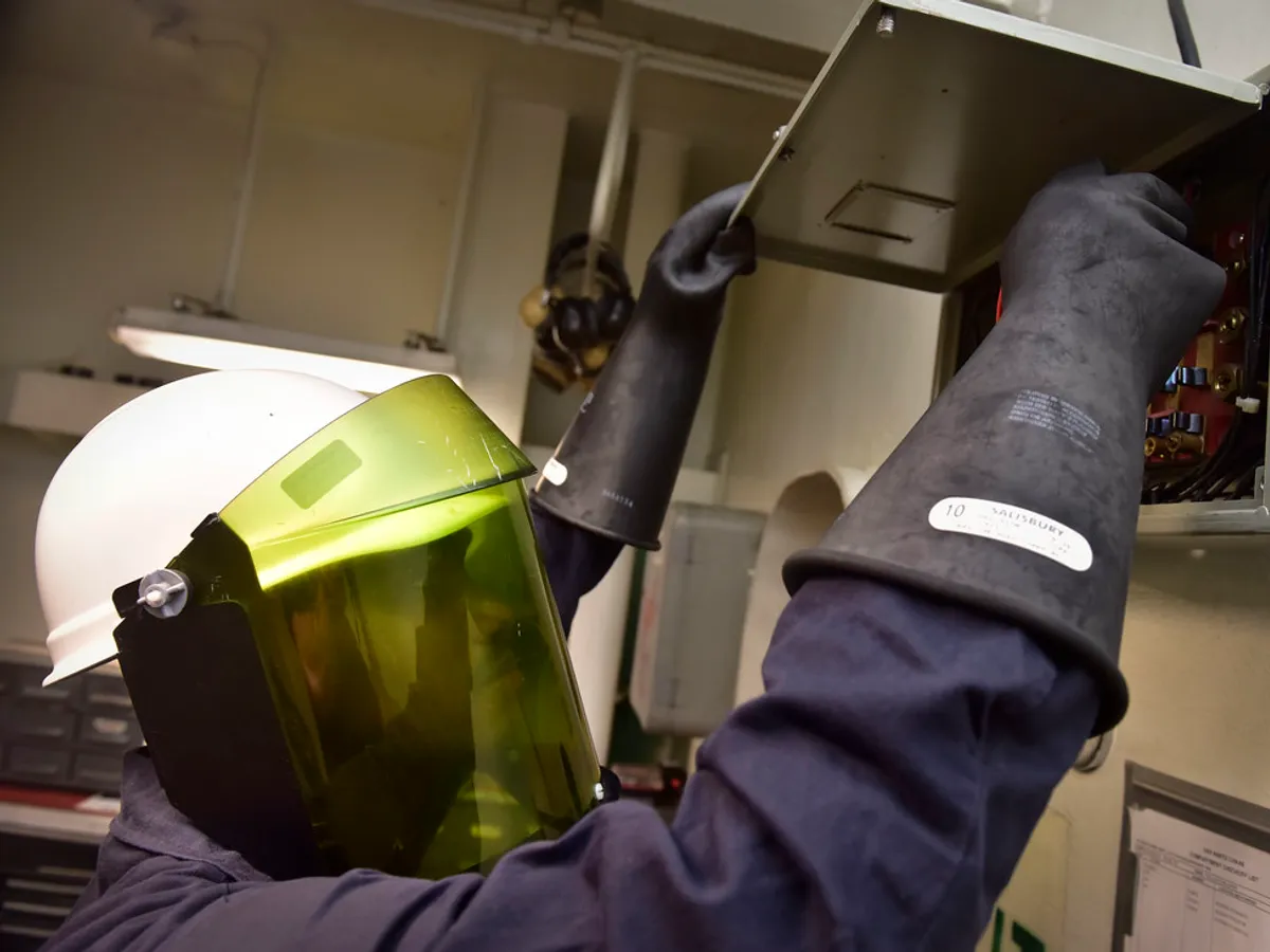 Electrician in protective gear working on an electrical panel